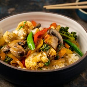 A vibrant bowl of vegetable stir-fry with rice, featuring mushrooms, broccoli, and bell peppers.