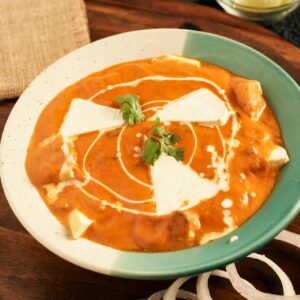 Creamy paneer makhani served in a bowl with onion rings and garnished with fresh herbs.