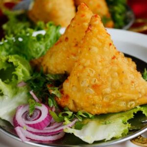 Close-up of crispy samosas served with fresh lettuce and onion rings.